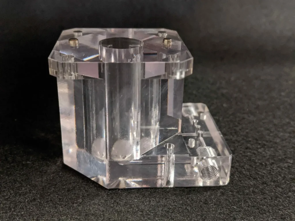 Clear machined polycarbonate housing with precision-drilled holes and threaded ports