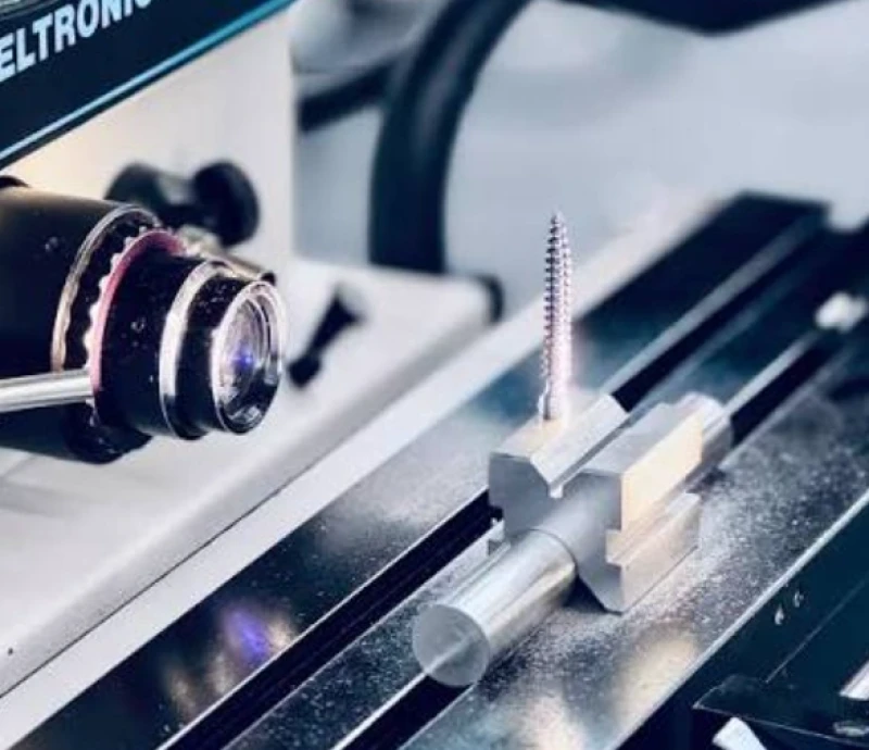 Optical comparator lens inspecting threaded micro-machined screw held in fixture