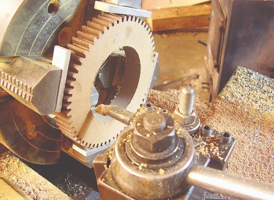 Machined phenolic gear on lathe fixture surrounded by cutting dust