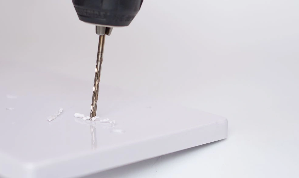 Power drill with drill bit boring into white polypropylene sheet 