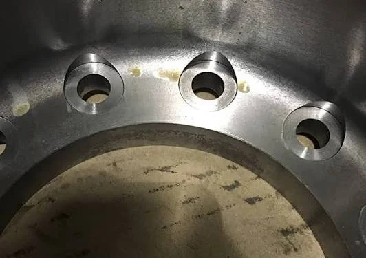 : Machined metal flange with several raised spotface bolt hole seats cut into a curved surface for flat fastener seating