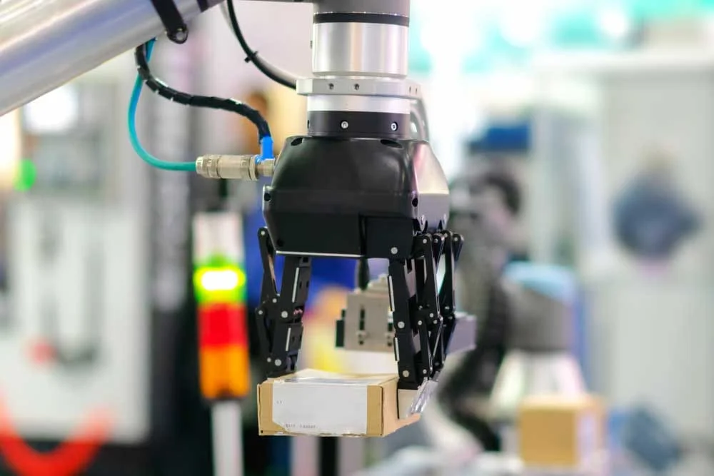 Robotic end effector with articulated gripper fingers grasping a small cardboard box.