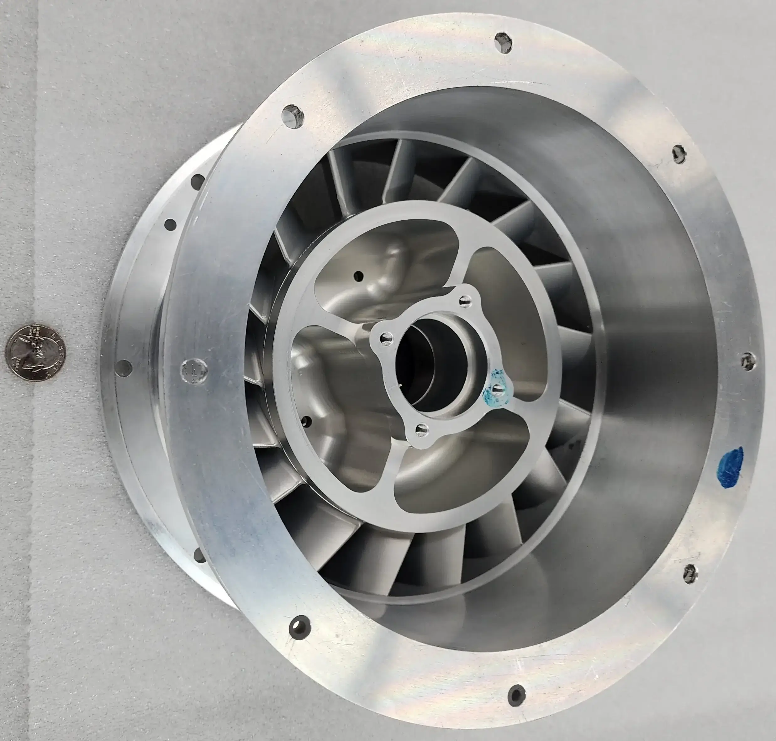 Machined turbine impeller with radial vanes and bolted flange, coin shown for scale