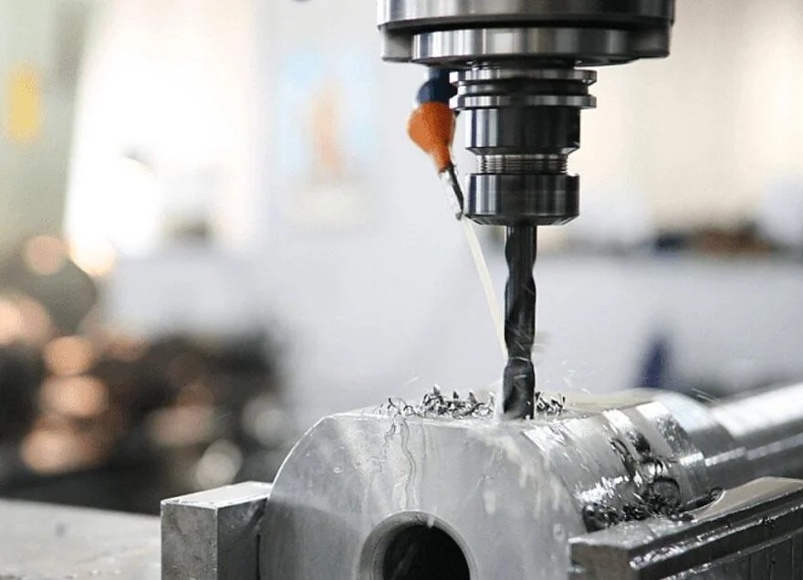 CNC drill bit boring into a steel workpiece with coolant and metal chips visible